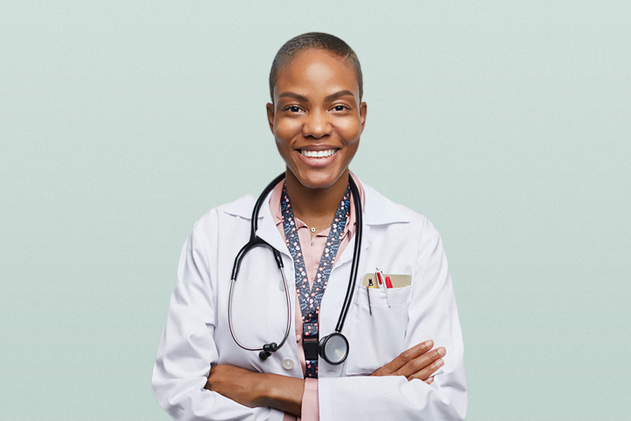 A middle-aged Black female doctor in a white lab coat with her arms folded, smiling against a pale blue background
